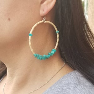 May include: Large hoop earrings made of natural beige material with turquoise stones. The earrings are a simple design with a circular shape.