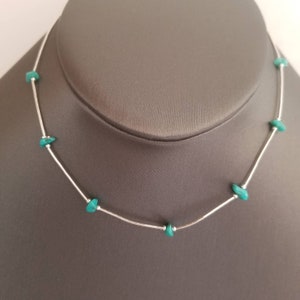 May include: A silver-toned necklace featuring a series of thin, smooth metal tubes separated by small, irregular, bright turquoise-colored stone chips. The design alternates between the metallic segments and the vibrant, raw-edged stone accents.