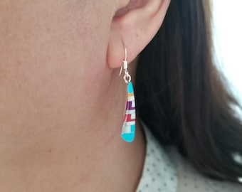 May include: A pair of dangle earrings with a turquoise, red, white and gold inlay design. The earrings are silver and have a teardrop shape.