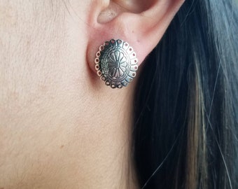 May include: Silver earrings with a floral design. The earrings are round and have a scalloped edge.