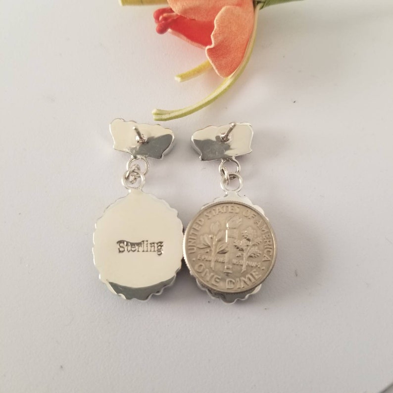 May include: A pair of silver dangle earrings with a round, textured design. The back of the earrings are stamped with "Sterling".
