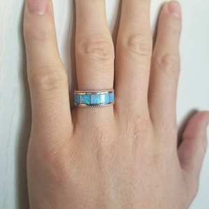 May include: A silver band ring with a row of light blue opal stones set in a gold band.