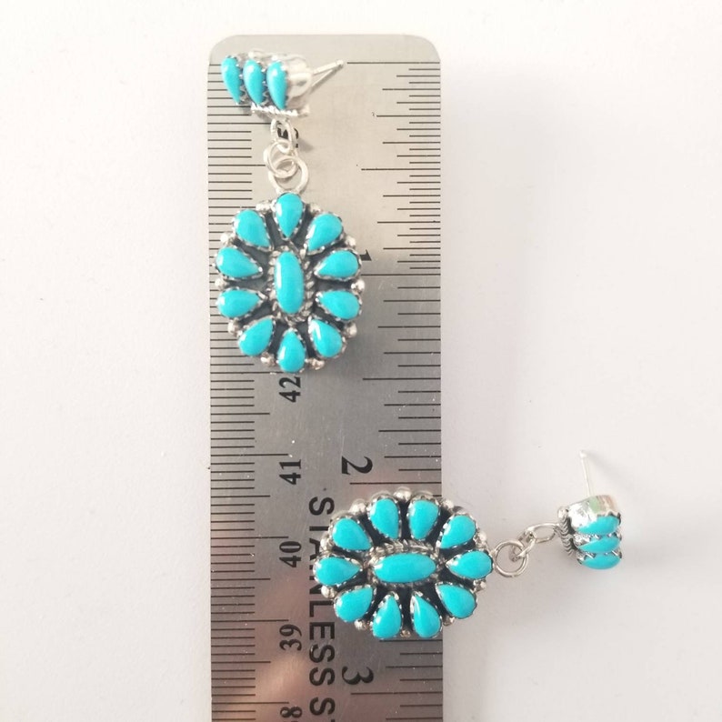May include: A pair of dangle earrings with turquoise stones set in silver. The earrings are approximately 5 cm long. The turquoise stones are a bright blue colour.
