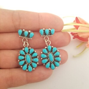 May include: A pair of dangle earrings with turquoise stones set in sterling silver. The earrings feature a cluster of turquoise stones in the shape of a flower, with a smaller cluster of turquoise stones at the top.