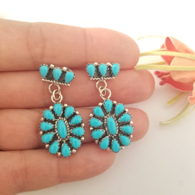 May include: A pair of dangle earrings with turquoise stones set in sterling silver. The earrings feature a cluster of turquoise stones in the shape of a flower, with a smaller cluster of turquoise stones at the top.