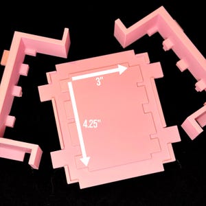 May include: Pink plastic mold with a 3 inch by 4.25 inch square opening. The mold is in pieces and is designed for making a square cake.