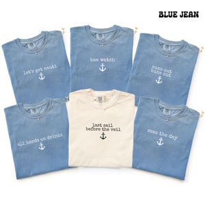 May include: Five blue t-shirts and one cream t-shirt featuring nautical-themed text and anchor graphics. The blue shirts display the phrases let's get nauti, bae watch, suns out buns out, all hands on drinks, and seas the day. The cream shirt says last sail before the veil.