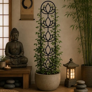 May include: A tall, black metal plant trellis featuring a repeating lotus flower design, positioned inside a round, light gray stone planter. The trellis supports a climbing green vine that grows vertically through the open metal frame.