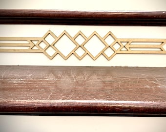 May include: A decorative wooden wall art piece with a geometric design. The art features a series of diamond and rectangular shapes, with a light brown color. The piece is mounted on a white wall above a dark brown wooden surface.