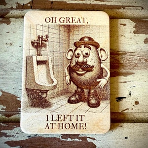 Puede incluir: Un letrero de madera con una imagen de dibujos animados de Mr. Potato Head de pie en un baño con un urinario. El letrero dice "Oh great, I left it at home!"