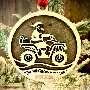 May include: A wooden Christmas ornament featuring a silhouette of Santa Claus riding an ATV with a bag of gifts. The ornament is brown and has the text "BEN 2024" on the bottom.