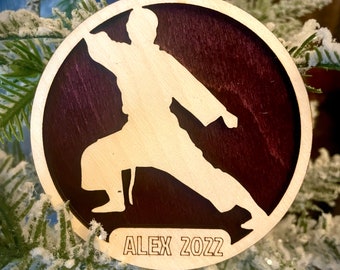 May include: A wooden Christmas bauble featuring a silhouette of a person in a karate pose. The bauble is painted in shades of brown and has the text "ALEX 2022" engraved on the bottom.