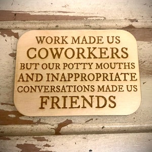 May include: A rectangular wooden sign with rounded corners. The sign has engraved text that reads: "WORK MADE US COWORKERS BUT OUR POTTY MOUTHS AND INAPPROPRIATE CONVERSATIONS MADE US FRIENDS."