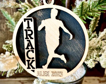 Peut inclure: Une décoration en bois noir et blanc avec une silhouette de coureur et le mot "TRACK" écrit verticalement. La décoration comprend également le nom "ALEX 2023".