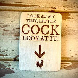 May include: A wooden sign with the text "Look at my tiny, little COCK Look at it!" and an arrow pointing down to a rooster illustration.