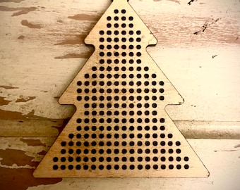 May include: A wooden Christmas tree ornament with a hole at the top for hanging. The ornament is made of light brown wood and has a grid of small holes throughout the surface.