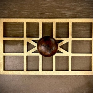 May include: A gold-colored metal frame with a grid pattern and a brown wooden knob in the center.