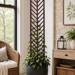 May include: A tall, dark purple wooden plant trellis with a vertical herringbone pattern and a rounded top arch. The trellis is inserted into a large, round, dark gray planter containing a green vining plant that grows upward along the structure.