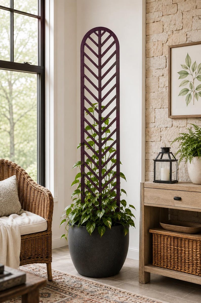 May include: A tall, dark purple wooden plant trellis with a vertical herringbone pattern and a rounded top arch. The trellis is inserted into a large, round, dark gray planter containing a green vining plant that grows upward along the structure.