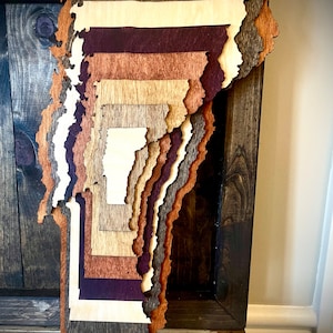 Puede incluir: Una pieza de arte de pared de madera en capas con forma del estado de Vermont. La madera est&aacute; te&ntilde;ida en varios tonos de marr&oacute;n, incluyendo marr&oacute;n oscuro, marr&oacute;n claro y marr&oacute;n rojizo. La pieza est&aacute; montada en un marco de madera marr&oacute;n oscuro.