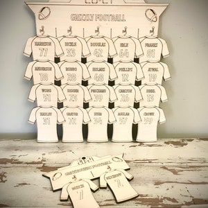 May include: A wooden football jersey holder with the text "Grizzly Football" and "20:21" at the top. The holder has 18 jersey slots with numbers and names printed on each slot. The bottom of the holder has a smaller wooden sign with the text "20:21 Grizzly Football" and two jersey slots with numbers.