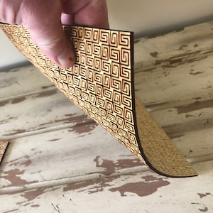 May include: A sheet of wood with a geometric pattern cut out of it. The wood is a light brown color and the pattern is a dark brown color.
