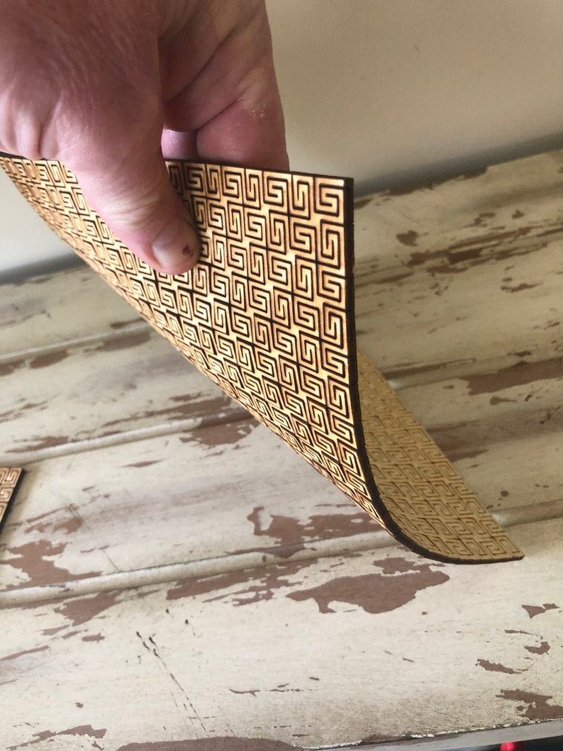 May include: A sheet of wood with a geometric pattern cut out of it. The wood is a light brown color and the pattern is a dark brown color.