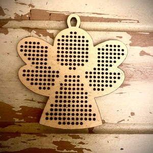 May include: A wooden angel ornament with a hole at the top for hanging. The angel is made of light brown wood and has a dotted pattern.