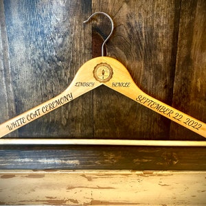 May include: A wooden hanger with the text "White Coat Ceremony" on one side and "Lindsey Henkle September 22, 2022" on the other side. The hanger has a small circular design in the centre.