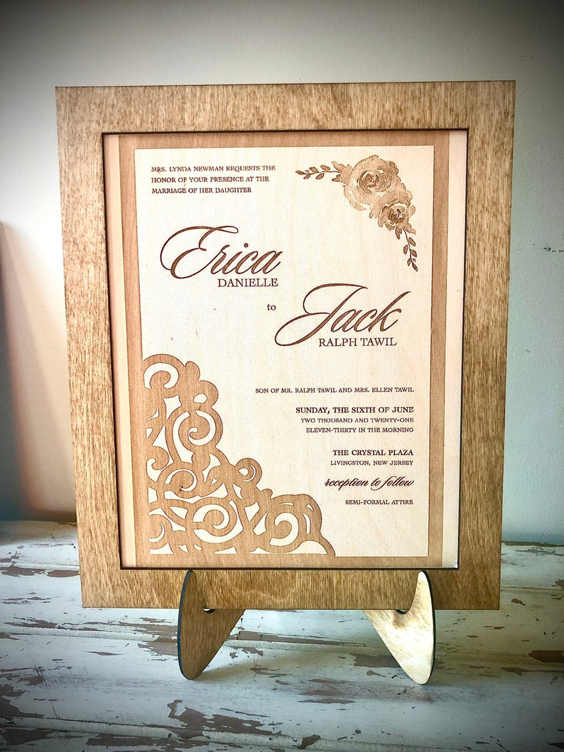 May include: A wooden laser-cut wedding invitation with a floral design and the text "Mrs. Lynda Newman requests the honor of your presence at the marriage of her daughter Erica Danielle to Jack Ralph Tawil Son of Mr. Ralph Tawil and Mrs. Ellen Tawil Sunday, the sixth of June two thousand and twenty-one eleven-thirty in the morning The Crystal Plaza Livingston, New Jersey reception to follow Semi-formal attire"