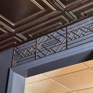 Puede incluir: Primer plano de un techo con un borde decorativo. El techo está hecho de azulejos marrones con un patrón en relieve. El borde está hecho de un material azul oscuro con un diseño geométrico dorado.