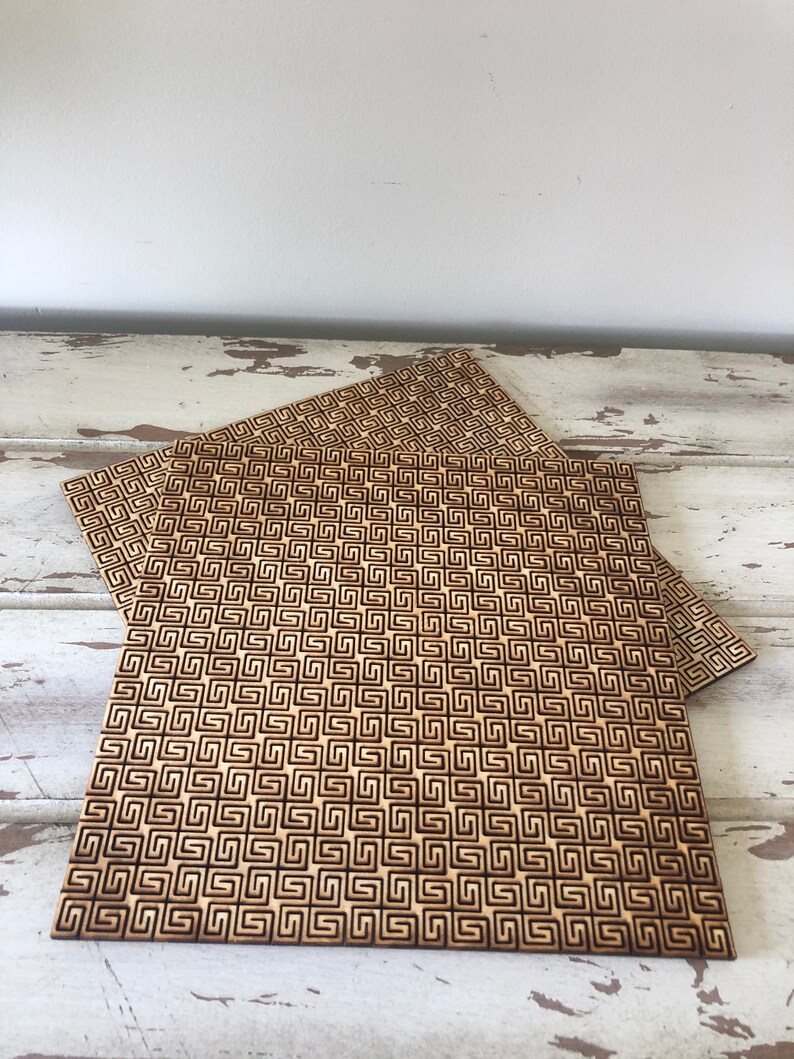 May include: Three wooden coasters with a geometric pattern. The coasters are made of light brown wood and have a dark brown geometric pattern.