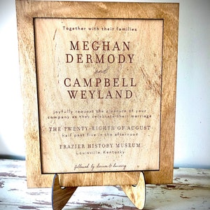 May include: A rustic wooden sign with a cream background and brown text announcing the wedding of Meghan Dermody and Campbell Weyland. The wedding will take place on August 28th at 5:30 PM at the Frazier History Museum in Louisville, Kentucky. The sign is followed by the text "followed by dinner & dancing."