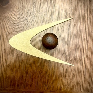 May include: A gold boomerang-shaped design with a brown sphere in the center, on a woodgrain background.