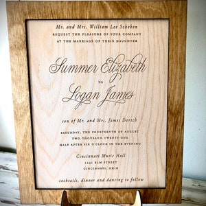 May include: A wooden wedding invitation with a brown frame and a light wood background. The invitation reads "Mr. and Mrs. William Lee Scheben request the pleasure of your company at the marriage of their daughter Summer Elizabeth to Logan James son of Mr. and Mrs. James Dortch Saturday, the fourteenth of August two thousand twenty-one half after six o'clock in the evening Cincinnati Music Hall 1141 BLM Street Cincinnati, Ohio cocktails, dinner and dancing to follow."