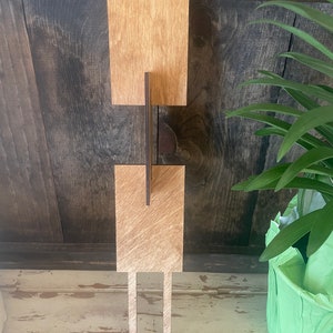 Op de afbeelding: Twee houten borden met een bruine vlek, elk met een gleuf om een kaart of foto in te steken. De borden zijn bevestigd aan twee houten palen, die in de grond worden gestoken.