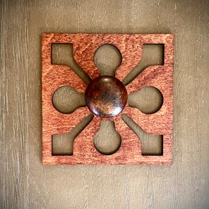 Puede incluir: Una decoración de pared cuadrada de madera con un diseño tallado y un pomo marrón en el centro.