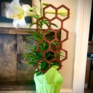 Pode incluir: Uma planta verde com flores brancas em um vaso verde com uma peça decorativa de madeira marrom em forma de favo de mel atrás.
