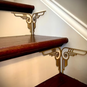 Puede incluir: Soportes de esquina decorativos de metal de color dorado con un diseño blanco y dorado, montados en una escalera pintada de blanco.