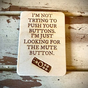 May include: Wooden sign with the text "I'M NOT TRYING TO PUSH YOUR BUTTONS. I'M JUST LOOKING FOR THE MUTE BUTTON." and a small image of a remote control.