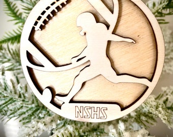 May include: A wooden ornament shaped like a football player running with a football. The ornament is painted in shades of brown and has the text "NSHS" engraved on the bottom.