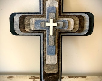 May include: A layered wooden cross with a white cross in the center. The cross is made of different shades of brown and gray wood.