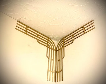 May include: Gold-colored metal corner trim with an Art Deco design. The trim is installed in the corner of a room, where the wall meets the ceiling.
