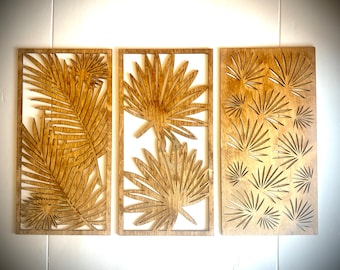 May include: Three wooden wall decor panels with a tropical leaf design. The panels are made of light brown wood and feature intricate cutouts of palm leaves.