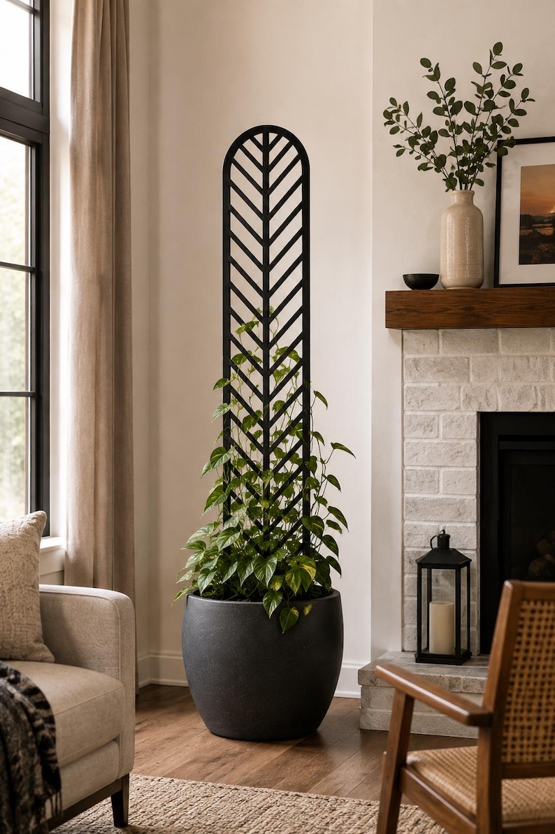 May include: A tall, black, arched plant trellis with a chevron pattern, supporting a green pothos plant in a large, round, dark gray planter. The trellis features a vertical frame with angled slats that create a repeating V-shaped design.