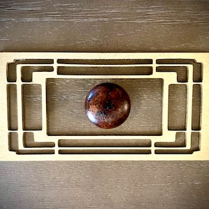 Może przedstawiać: Brązowy drewniany gałka z geometrycznym wzorem znajduje się w ozdobnej ramie wykonanej z jasnego drewna.