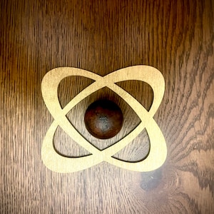 May include: A gold-colored metal atom symbol with a dark brown sphere in the center.