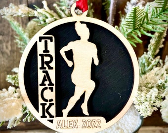 Peut inclure: Une décoration en bois noir et blanc avec une silhouette de coureur et le mot "TRACK" écrit verticalement sur le côté gauche. La décoration est personnalisée avec le nom "ALEX 2022".