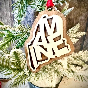 Adorno de madera cortado con láser de dos capas con diseño de palabras de Maine. Etiqueta de regalo de Maine disponible sin terminar o con 11 opciones de acabado adicionales.