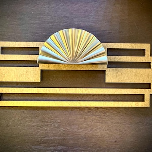May include: A gold-colored metal door pull with a decorative, fan-shaped design. The pull is mounted on a rectangular, gold-colored metal plate.